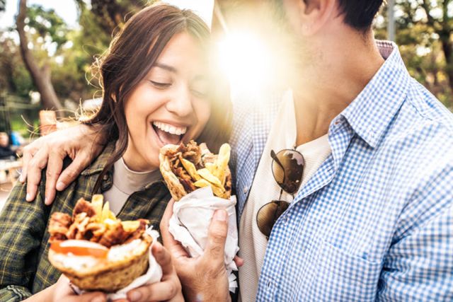 Ein Pärchen sitzt gemeinsam im sonnigen Grünen und kostet gegenseitig unwiderstehliche Dönergerichte.